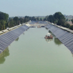 Lined canal partially filled with water extends into the distance. Photo by NAUE.