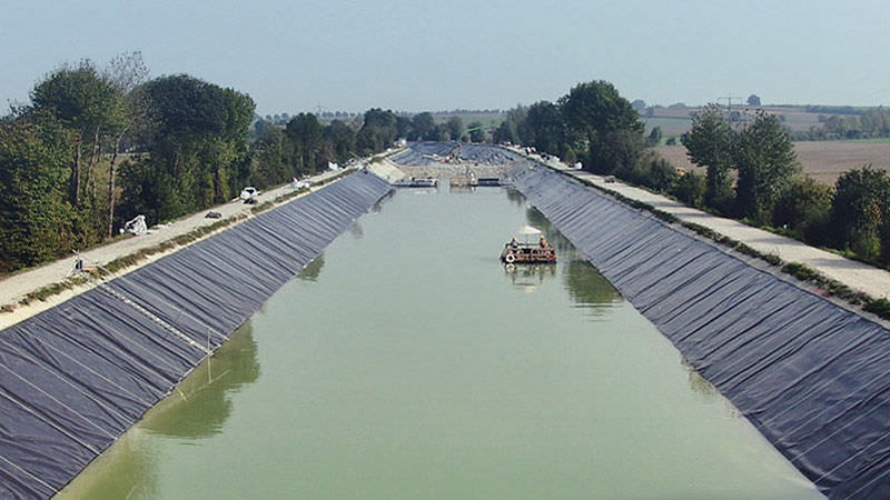 Lined canal partially filled with water extends into the distance. Photo by NAUE.
